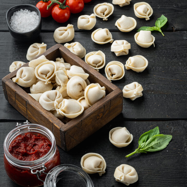 Tasty raw tortellini with flour and basil set, on black wooden table background , with copyspace  and space for text